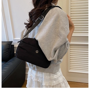 Detail of adjustable strap and metal logo on a black nylon crossbody bag worn by a model