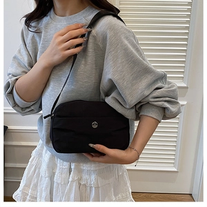 Detail of black nylon crossbody bag with silver logo worn with casual outfit