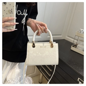Close-up of white snake-embossed leather handbag with woven handle and gold hardware