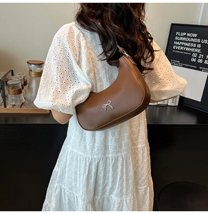 Detail of a brown crescent shoulder bag with silver bow buckle worn on a lace dress