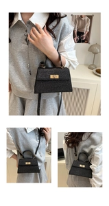 Detail of a black glitter trapezoid handbag with gold twist lock and adjustable shoulder strap