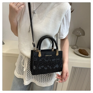 Detail of black stone-pattern shoulder bag with woven handle and gold metal hardware