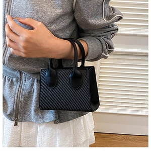 Dettaglio della mini borsa nera con goffratura saia tenuta da una modella in ambiente minimal