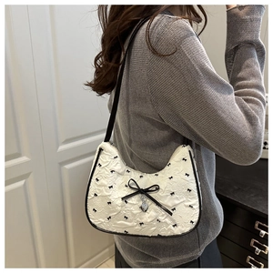 Detail of white hobo bag featuring 3D textured fabric and black ribbon bow with heart charm