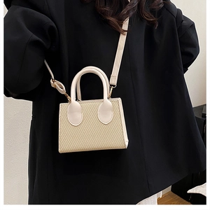 Dettaglio borsa a tracolla in paglia con finiture in pelle crema su blazer nero