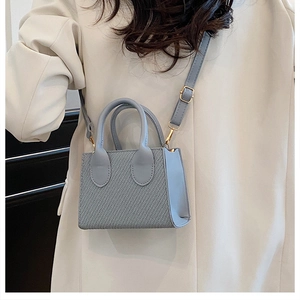 Dettaglio borsa a mano grigio-blu intrecciata con finiture dorate e blazer avorio chic