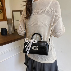 Detail of black glossy handbag with metal G buckle and delicate white lace bow accent