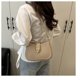 Close-up of beige half-moon underarm bag with gold metal buckle shown on shoulder