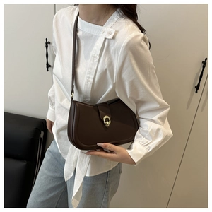 Detail of a dark brown leather crescent shoulder bag with golden round hardware clasp
