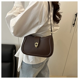 Detail of dark brown saddle bag with golden magnetic clasp worn by a model