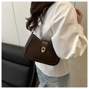 Detail of dark brown leather crescent bag with gold buckle on a model shoulder