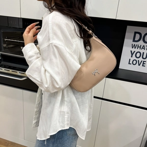 Elegant beige hobo bag with silver bow detail worn as a stylish shoulder underarm bag