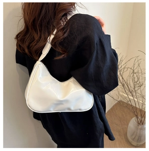 Detail of white glossy patent leather hobo bag worn by model in minimalist setting