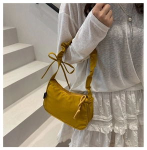 Close-up of mustard yellow shoulder bag with bow detail and pleated strap on model