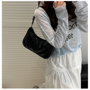 Detail of glossy black hobo shoulder bag with adjustable strap and polished patent leather
