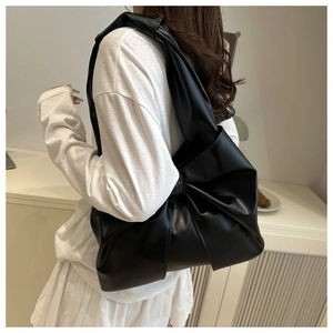 Close-up of a large black faux leather tote bag featuring a unique knotted shoulder strap
