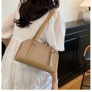 Close-up of warm brown minimalist shoulder bag featuring double adjustable straps and gold logo
