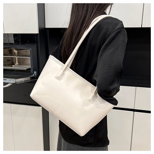 Minimalist beige leather tote bag shown on model in a modern interior setting