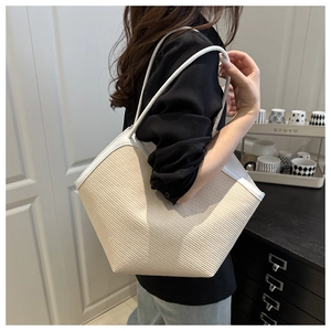 Detail of a woven straw tote bag with white leather straps worn by a model