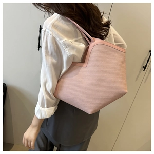 Side view of a pink geometric woven straw tote bag held by a model in a minimalist room