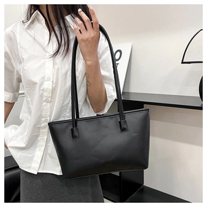 Minimalist black tote bag with long handles shown in a modern interior setting