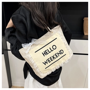 Detail of woven straw tote bag featuring Hello Weekend print and white lace bow detail