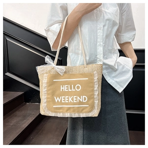 Detail of straw tote bag with HELLO WEEKEND canvas patch and white lace edges