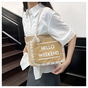 Detail of straw woven tote bag featuring HELLO WEEKEND canvas patch and lace bow trim