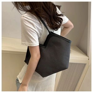 Side view of dark grey straw woven tote bag worn on shoulder in a bright interior