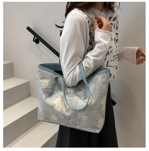 Detail of light blue tote bag with white floral pattern and leather shoulder strap
