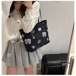 Detail of black tote bag featuring white floral patterns and gold rivet hardware accents