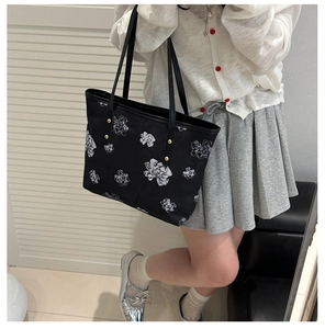Detail of black canvas tote bag with white floral patterns and gold metal rivets