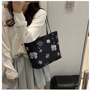 Detail of black tote bag with white floral pattern and gold rivets on the handle