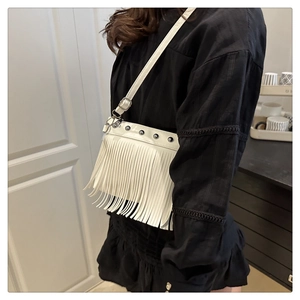 Détail d'un sac bandoulière blanc orné de clous métalliques et de longues franges