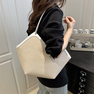 Chic beige straw tote bag with white leather trim shown on a shoulder in home setting