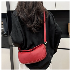 Red pebbled leather half-moon crossbody bag shown on model in a minimalist setting