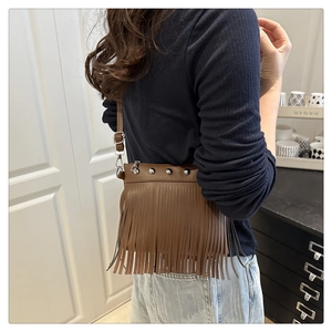 Detail of a brown fringe bucket bag with silver studs worn as a crossbody by a model