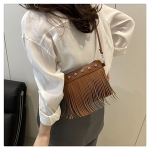 Detail view of brown leather bag with silver rivets and long fringe tassels on a model