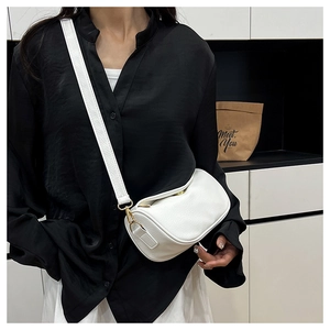 Detailed close-up of white lychee leather cylinder bag with wide strap and gold hardware