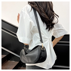Detail of black pebbled leather crossbody bag with gold hardware on white shirt
