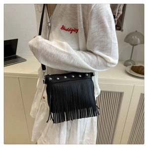 Detail of black crossbody bucket bag with silver studs and long fringe tassels
