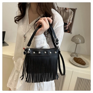 Detail of black fringe handbag with silver studs held by a model in a minimal setting