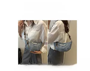 Dettaglio borsa a mezzaluna in denim azzurro con catena di perle e tracolla in pelle