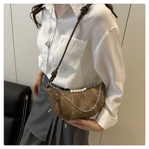 Dettaglio di una borsa a mezzaluna in camoscio marrone con perle bianche e catene d'argento