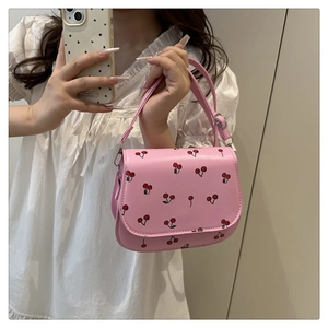 Detail of pink saddle bag featuring red cherry prints and adjustable shoulder strap