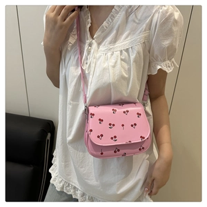 Close-up of a pink cherry print crossbody bag worn by a model in a summer lifestyle setting