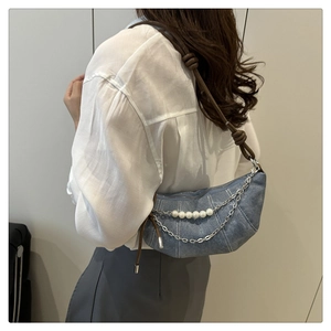 Detail of blue denim crescent bag with stylish pearl strings and silver metal chains