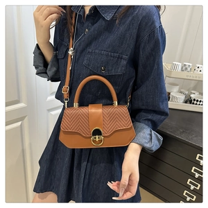 Detail of a two-tone leather crossbody bag featuring a textured flap and gold rotary lock