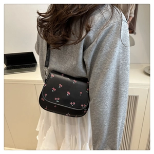 Detail of a chic black shoulder bag featuring vibrant cherry prints and adjustable strap