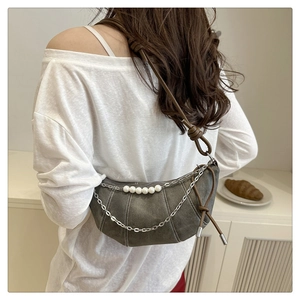 Detail of grey crescent bag featuring decorative metal chain, white pearls and brown strap